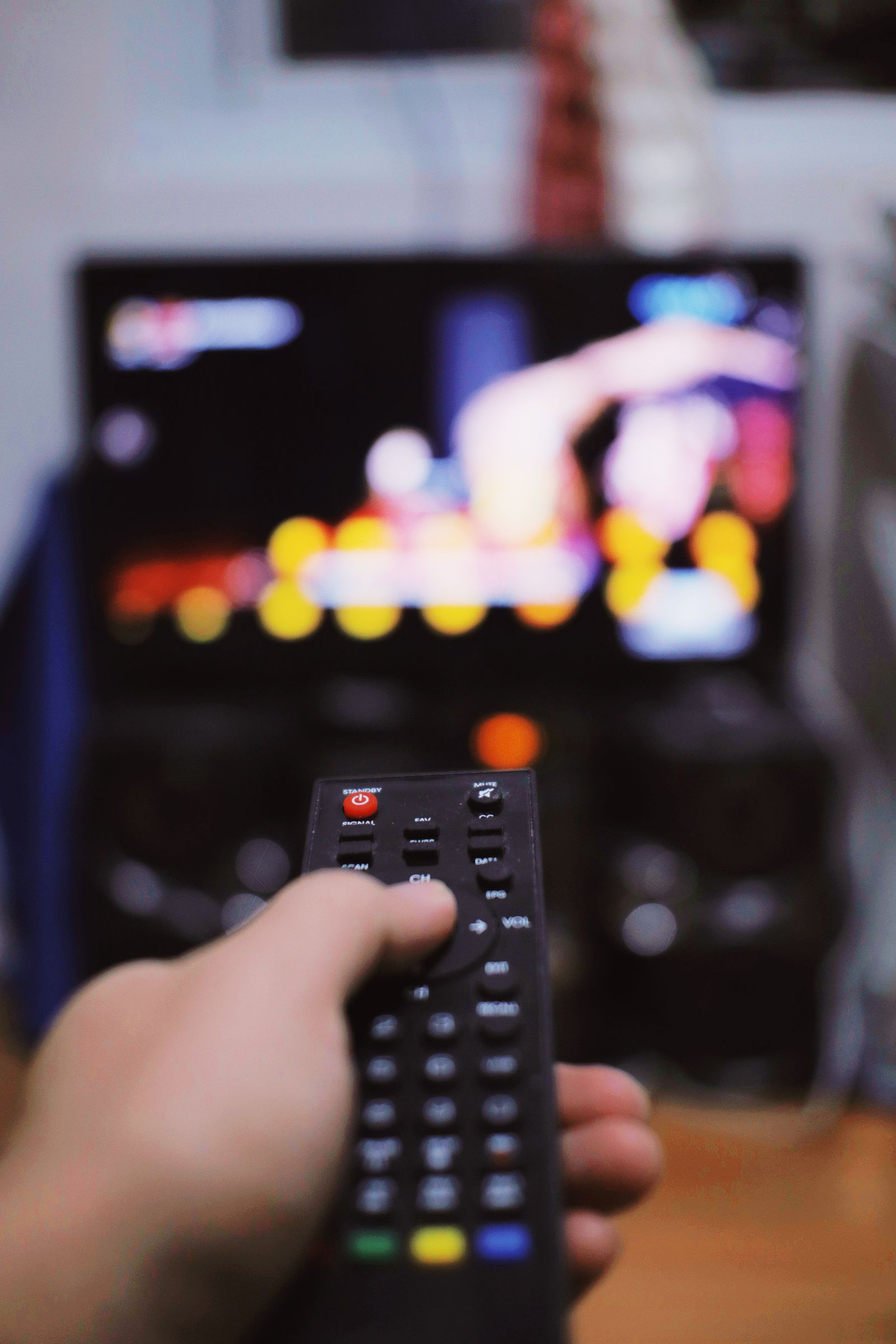 Hand using a television remote in front of a TV screen